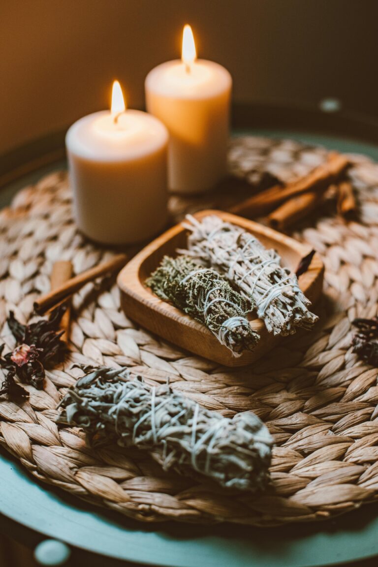 Bundles of sage and lit candles atop a woven placemat.