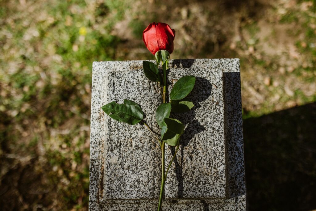 A red rose on top of a grave stone.